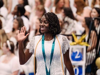 Nursing graduate waving as she walks after receiving her pin.