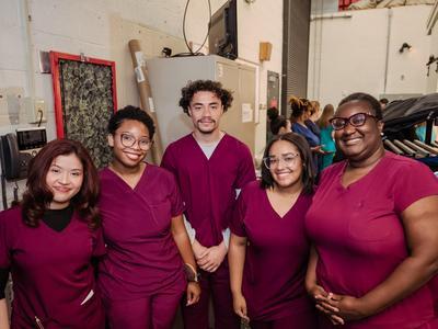 C.E.W.D. graduates in red scrubs posing together.