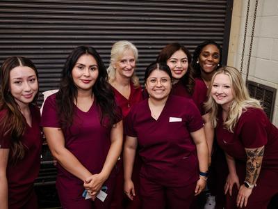 C.E.W.D. graduates in dark red scrubs posing together.