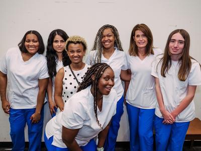 C.E.W.D. graduates in white and blue scrubs posing together.