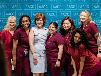 C.E.W.D. graduates in red scrubs posing together with another person.