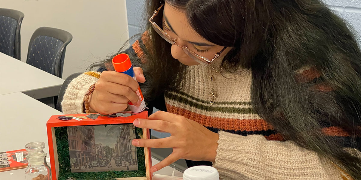 A student works on building a curiosity cabinet out of a cigar box.