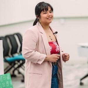 A student stands in front of a classroom presenting her business pitch.