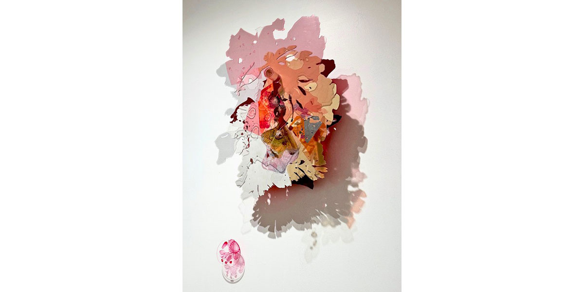 Artwork featuring layered, irregularly shaped pieces in shades of pink, red, beige, and gray, casting complex shadows