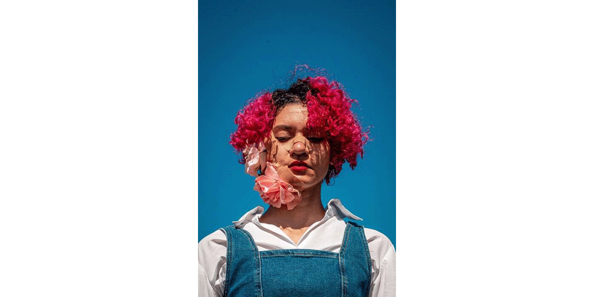 A woman with pink hair with flowers on her face and a band aid across her nose.