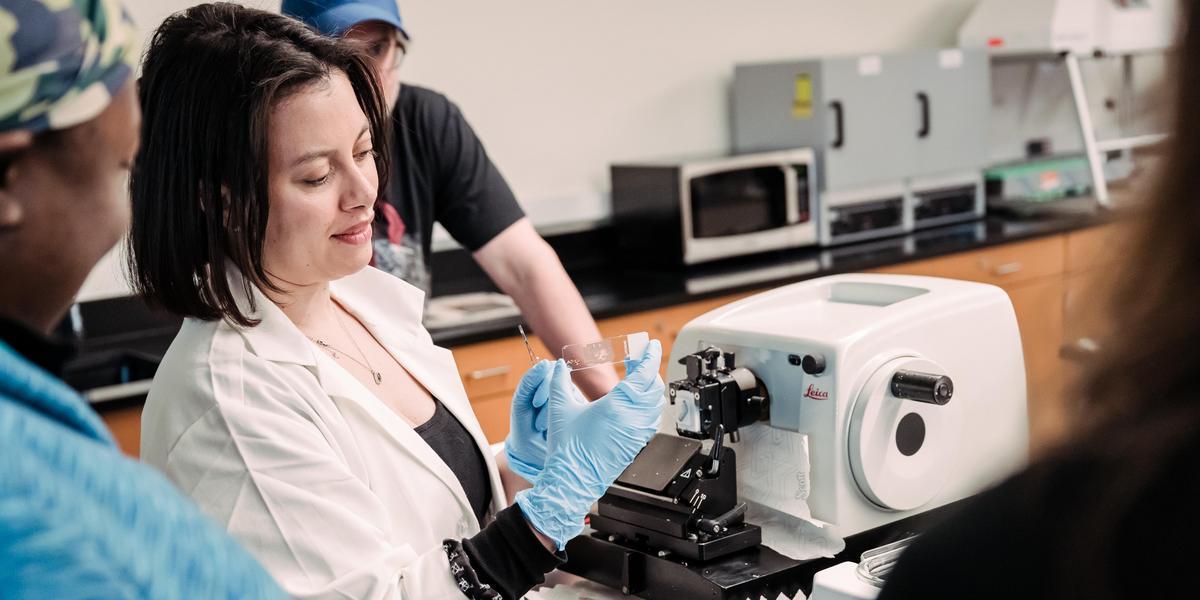 Histotechnician professor showing a slide to a student next to machine