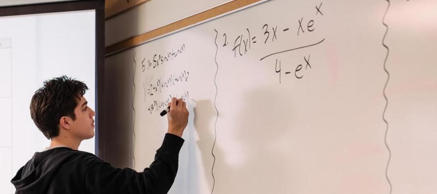 A student solves a math equation on a dry erase board.