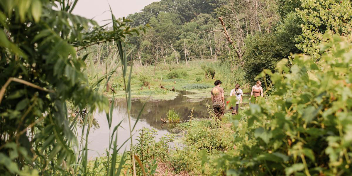 Three students walking near the water at a park surrounded my lots of greenery