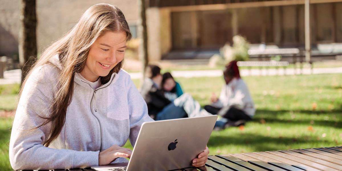 AACC student outside on campus on laptop.