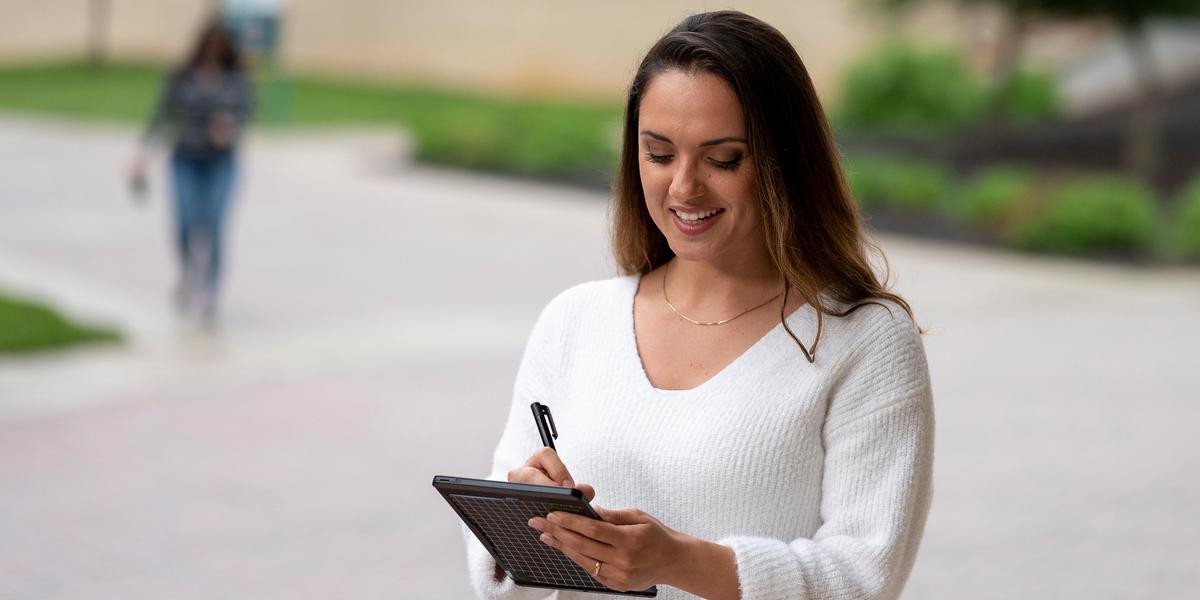 Student outside writing on tablet.